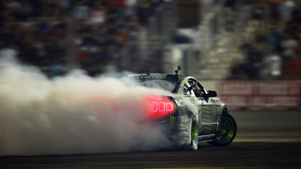 Ford Mustang drifting on racetrack with multiple cameras producing thick smoke cloud wallpaper