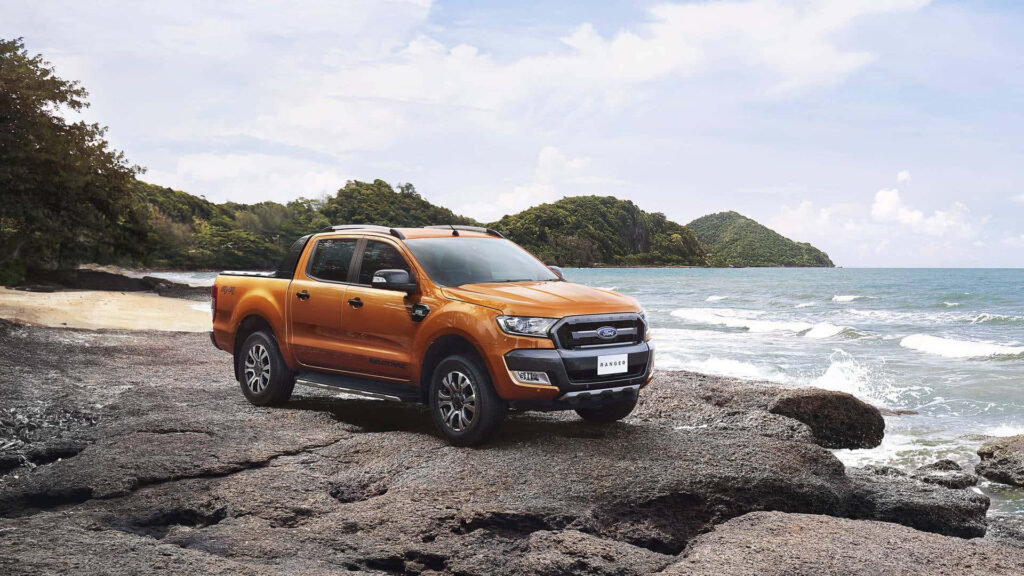 Ford Ranger on rugged coastal rocks with sea and green hills showcasing off-road power Wallpaper