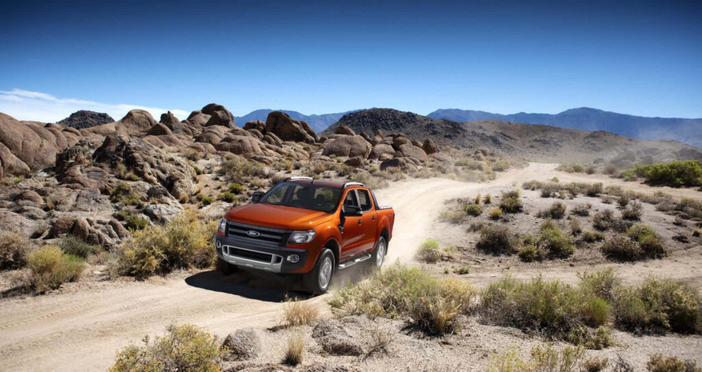 Ford Ranger Raptor off-road driving on rocky desert dirt road under clear blue sky wallpaper