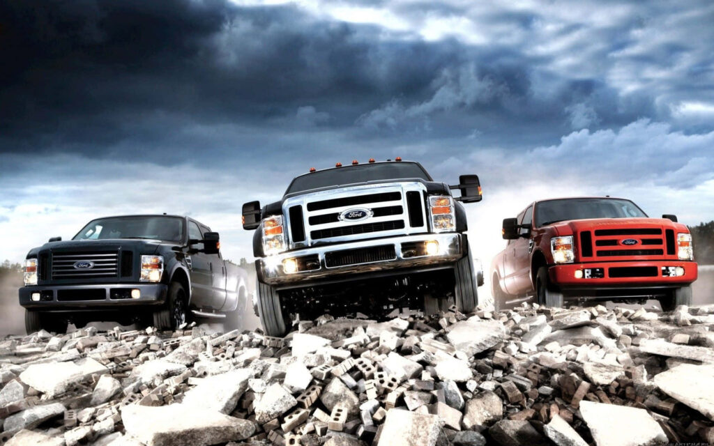 Three rugged Ford trucks driving over broken concrete under dramatic cloudy sky wallpaper background
