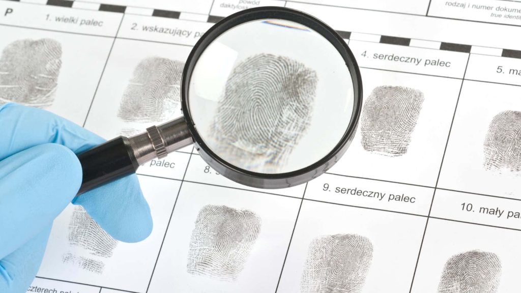 Forensic expert in blue gloves examining fingerprint identification card with magnifying glass close-up Wallpaper