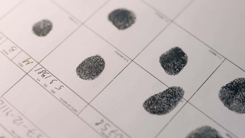High-angle photo of forensic fingerprint card with black ink prints and handwritten details on white paper Wallpaper