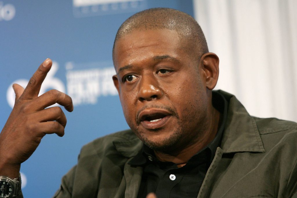 Forest Whitaker speaking during interview in dark jacket blue press backdrop wallpaper background
