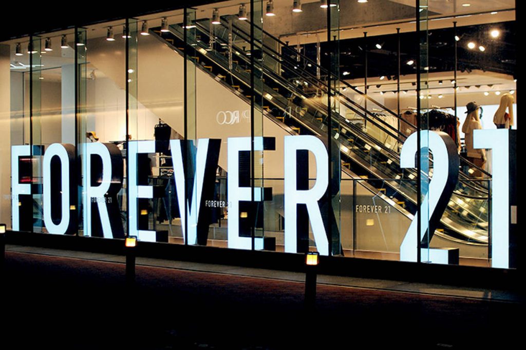 Forever 21 store facade at night with illuminated white logo escalator and clothing displays interior Wallpaper