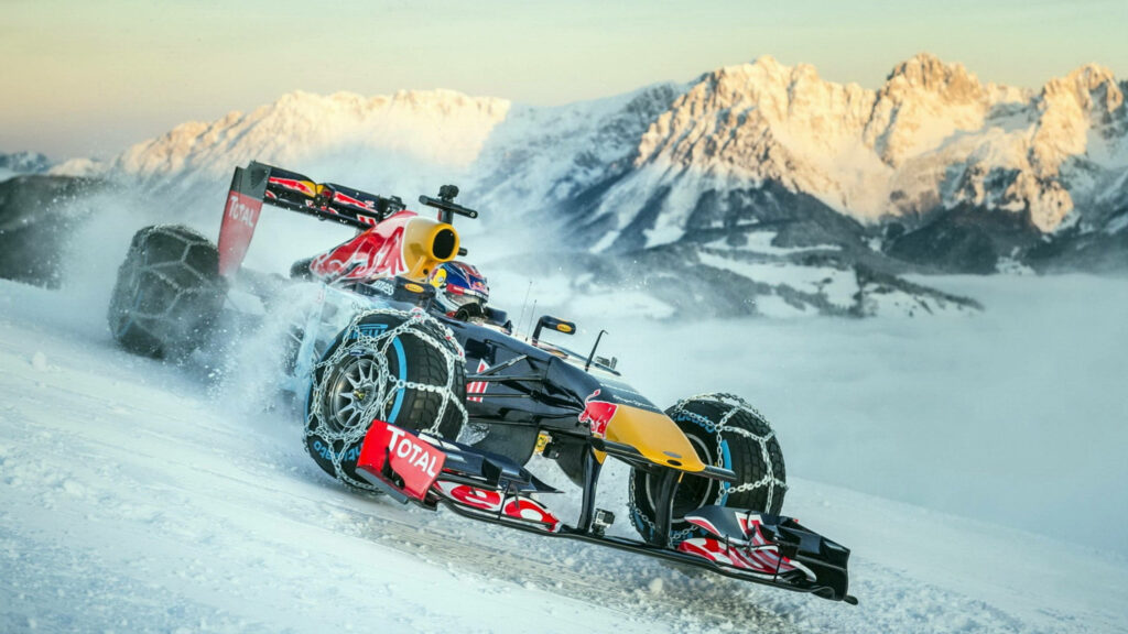 Formula 1 car racing on snowy mountain road with tire chains and snow-capped peaks background Wallpaper