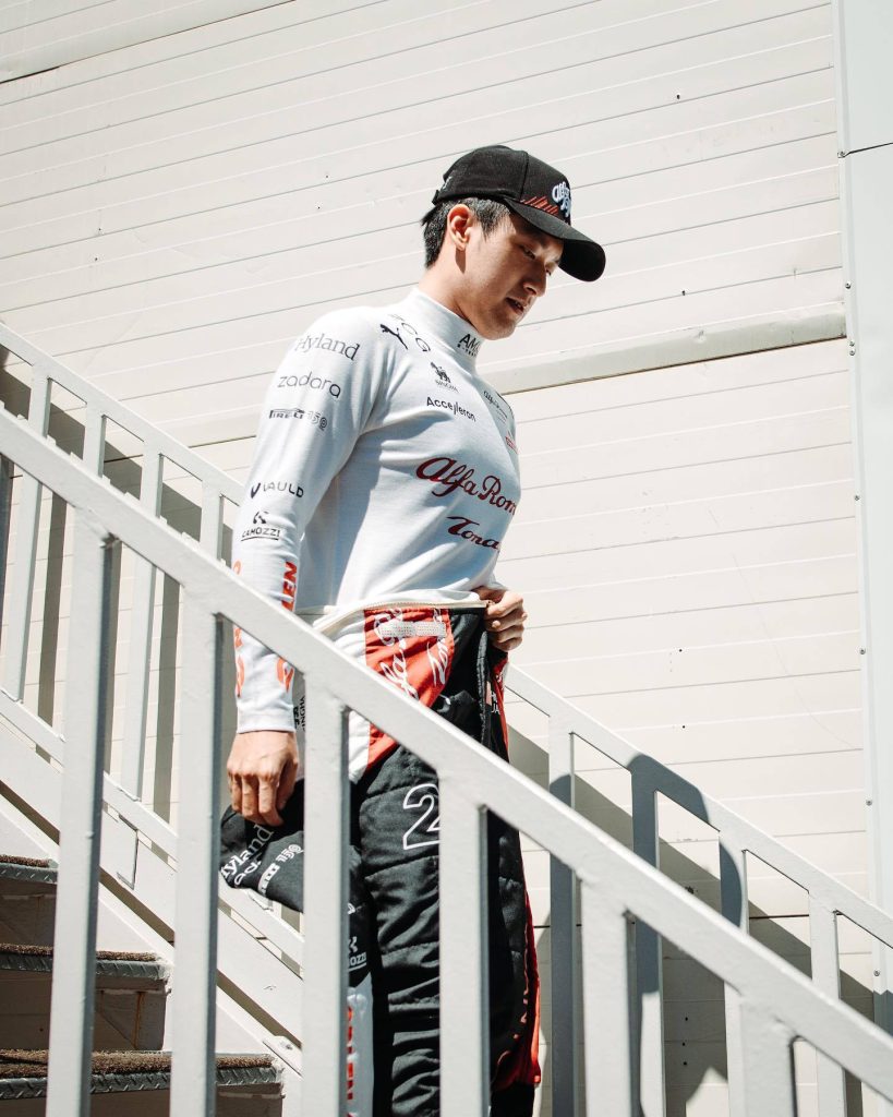 Formula 1 driver Zhou Guanyu in white Alfa Romeo racing suit descending stairs in sunlight wallpaper