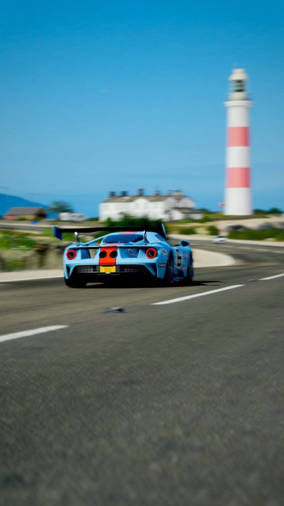 Ford GT racing fast on coastal highway near red white lighthouse Forza Horizon 4 wallpaper