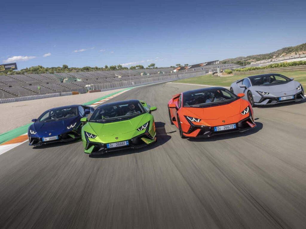 Four vibrant Lamborghinis racing side by side on racetrack with sleek design in stadium background Wallpaper