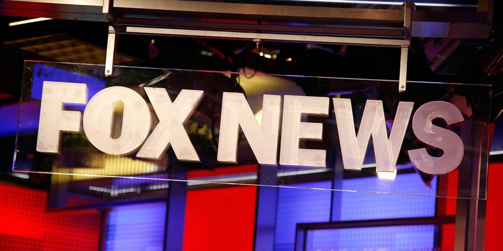 Fox News logo on transparent sign with vibrant red blue blurred TV studio background wallpaper