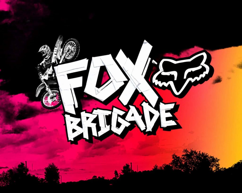 Motocross rider mid-air with Fox Brigade logo on vibrant pink and orange sunset wallpaper background