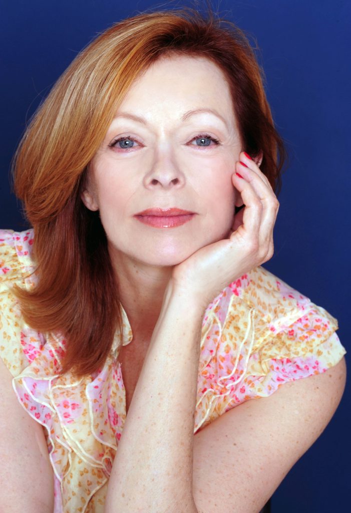 Frances Fisher studio portrait wearing yellow pink floral blouse with auburn hair navy background Wallpaper