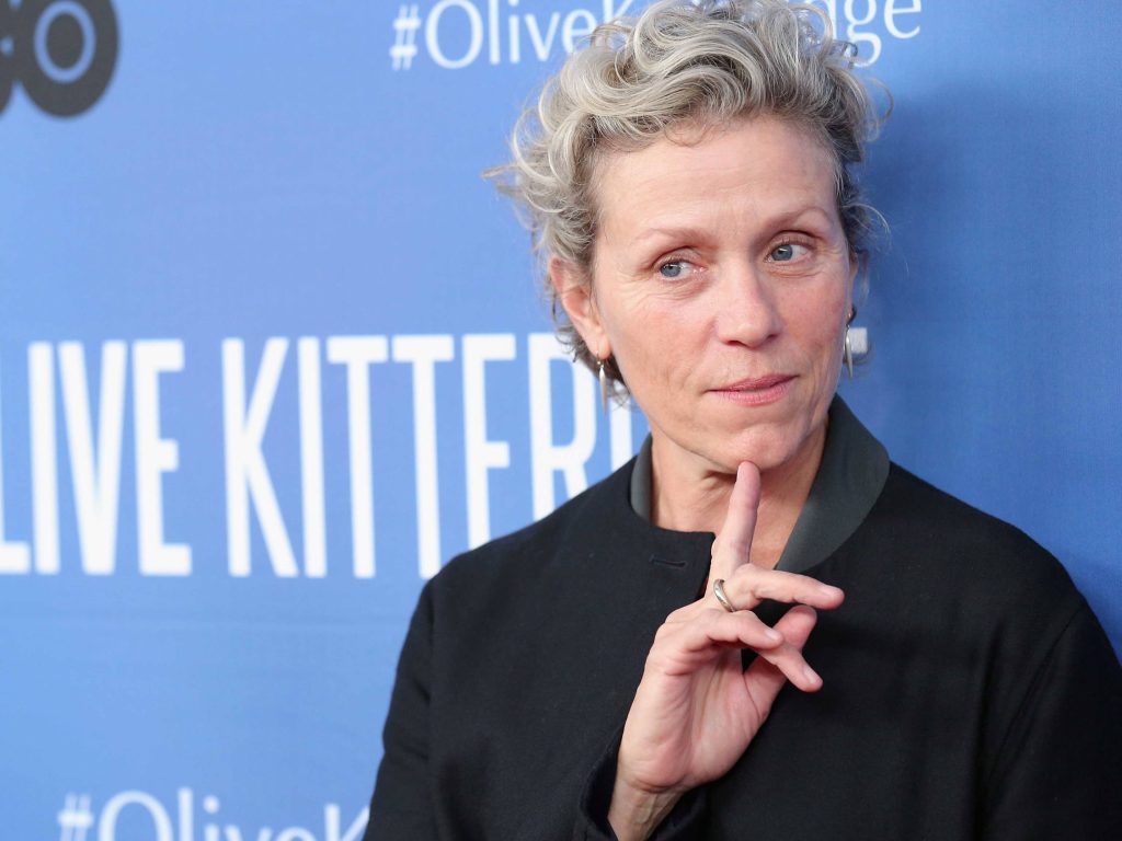 Actress Frances McDormand in dark jacket poses thoughtfully at Olive Kitteridge event backdrop Wallpaper