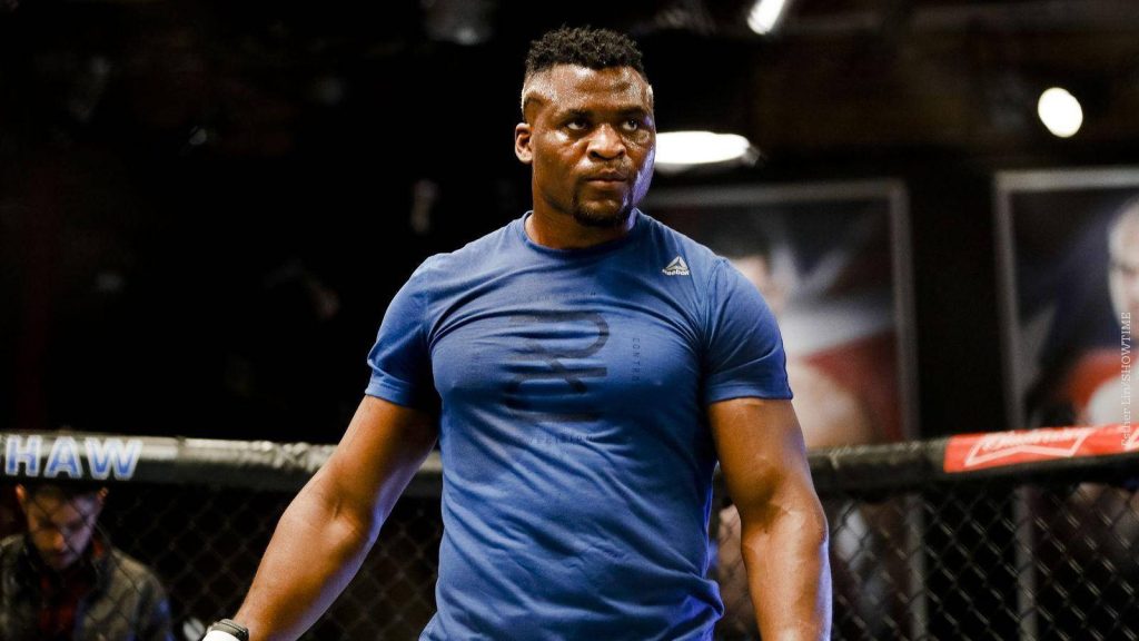 Francis Ngannou intense focused in blue Reebok shirt training dim gym wallpaper background