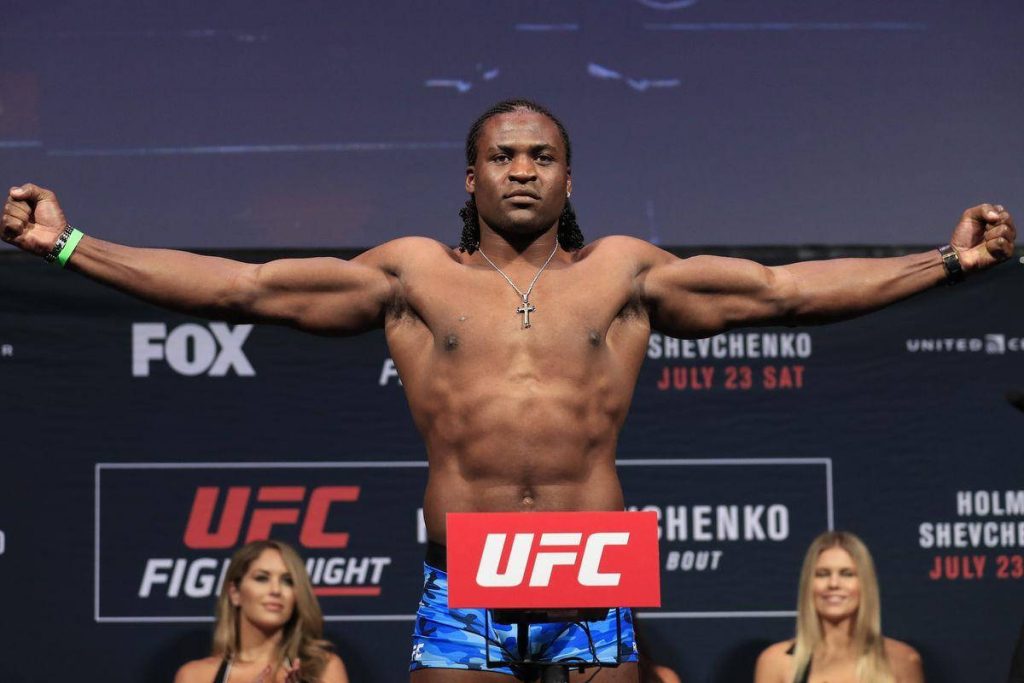 Francis Ngannou UFC heavyweight posing arms spread blue camo shorts silver cross necklace backdrop Wallpaper