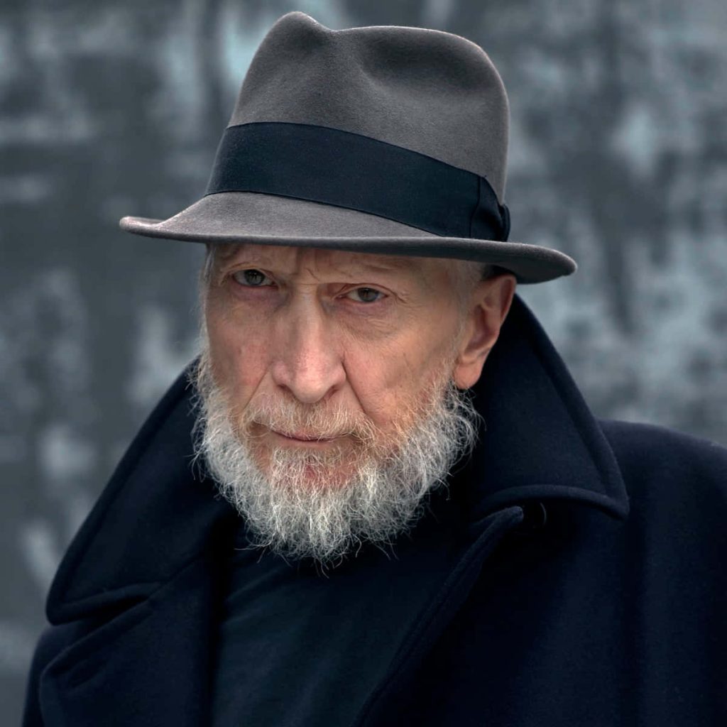 Frank Miller portrait wearing gray fedora and dark coat noir style wallpaper background