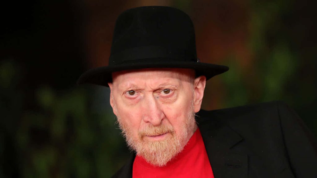 Portrait of comic book writer Frank Miller in black fedora and red shirt with blurred background Wallpaper