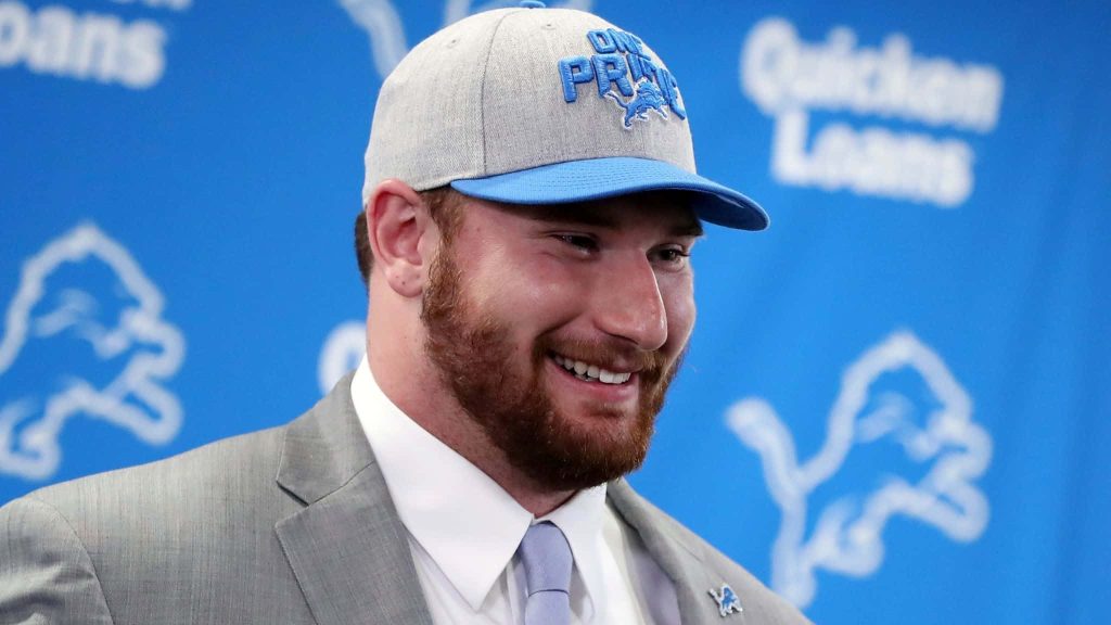 Detroit Lions NFL star Frank Ragnow in gray suit smiling at press conference with team backdrop Wallpaper