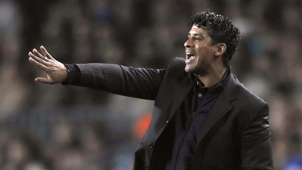 Frank Rijkaard coaching passionately in dark suit blurred stadium background wallpaper
