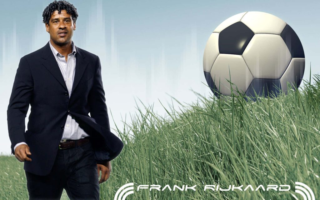 Frank Rijkaard in dark suit on grassy field with large soccer ball digital wallpaper background