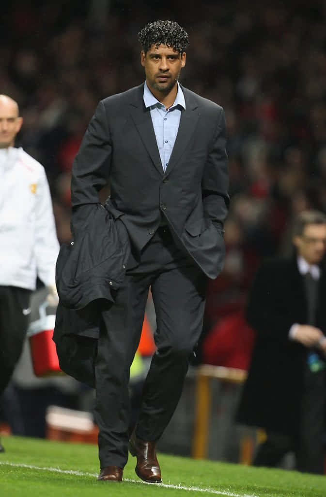 Frank Rijkaard walking football pitch in dark suit with blurred stadium background wallpaper