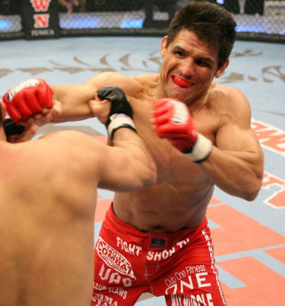 Frank Shamrock mid-strike in Strikeforce MMA cage wearing red gear and gloves wallpaper background