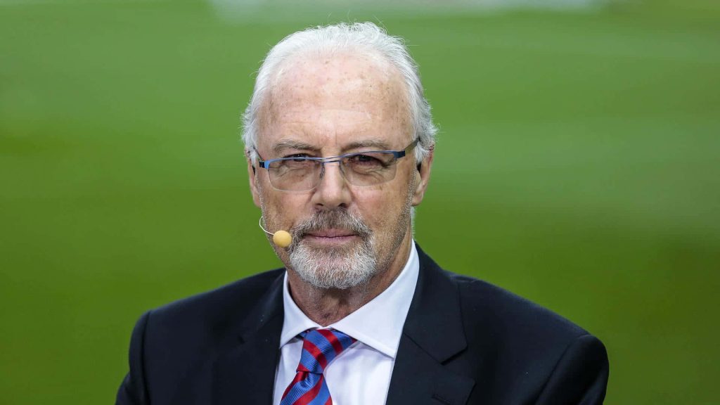 Franz Beckenbauer portrait in suit with headset at stadium celebrating German football legend Wallpaper