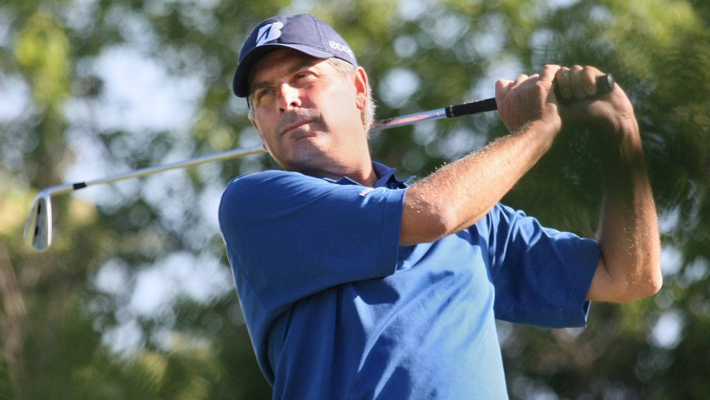 Golf legend Fred Couples in blue polo mid-swing with Bridgestone cap lush green background wallpaper