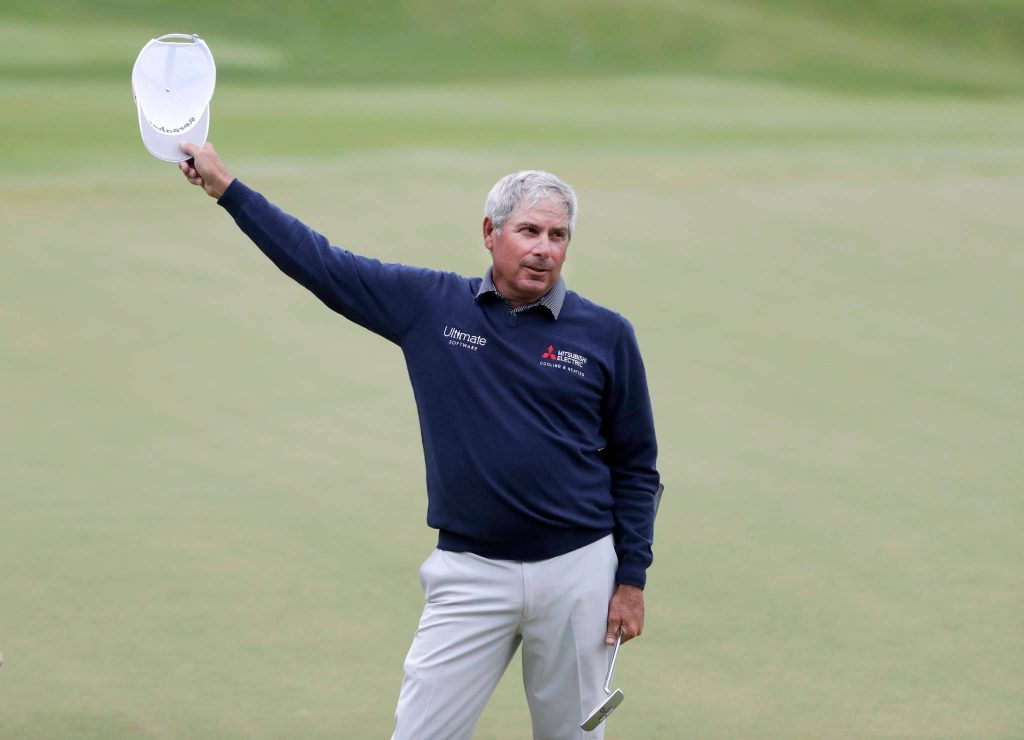 Professional golfer Fred Couples on putting green holding white cap wearing navy sweater and holding putter Wallpaper