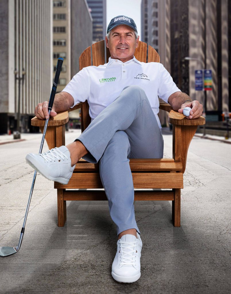 Fred Couples seated on Adirondack chair holding golf club in urban street with skyscrapers background Wallpaper