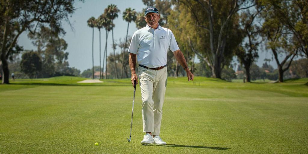 Fred Couples golfer in white polo holding club on sunny green fairway with palm trees background Wallpaper