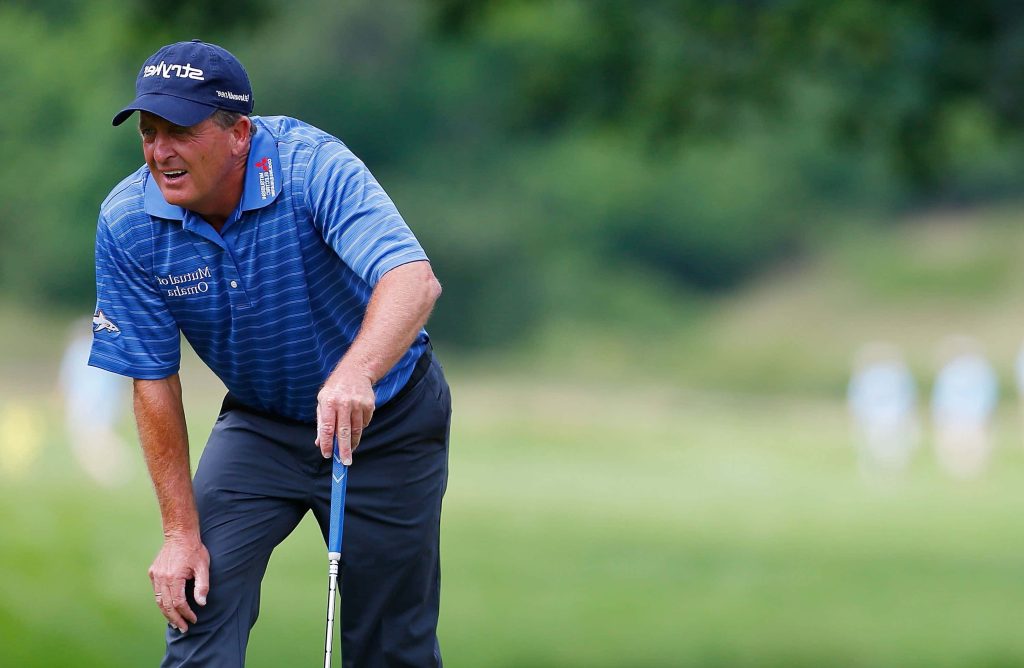 Professional golfer Fred Funk in blue polo and Srixon cap leaning on club on golf course Wallpaper