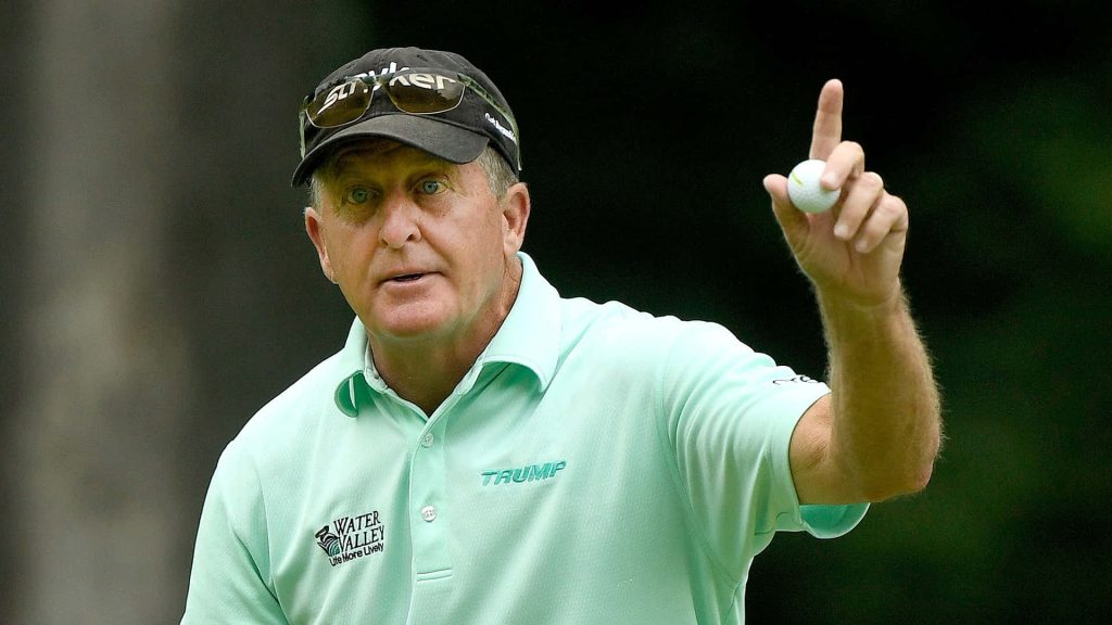 Professional golfer Fred Funk holds golf ball wearing green polo and black cap on golf course Wallpaper