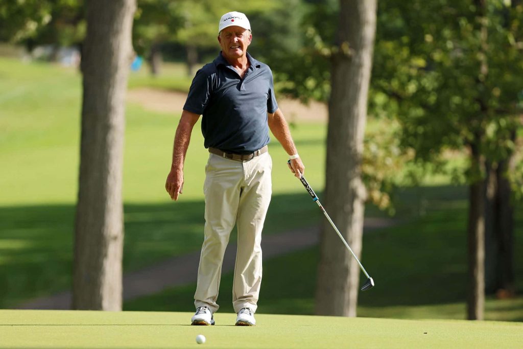 Fred Funk standing on sunny golf course green with putter near ball in navy polo and khaki pants Wallpaper