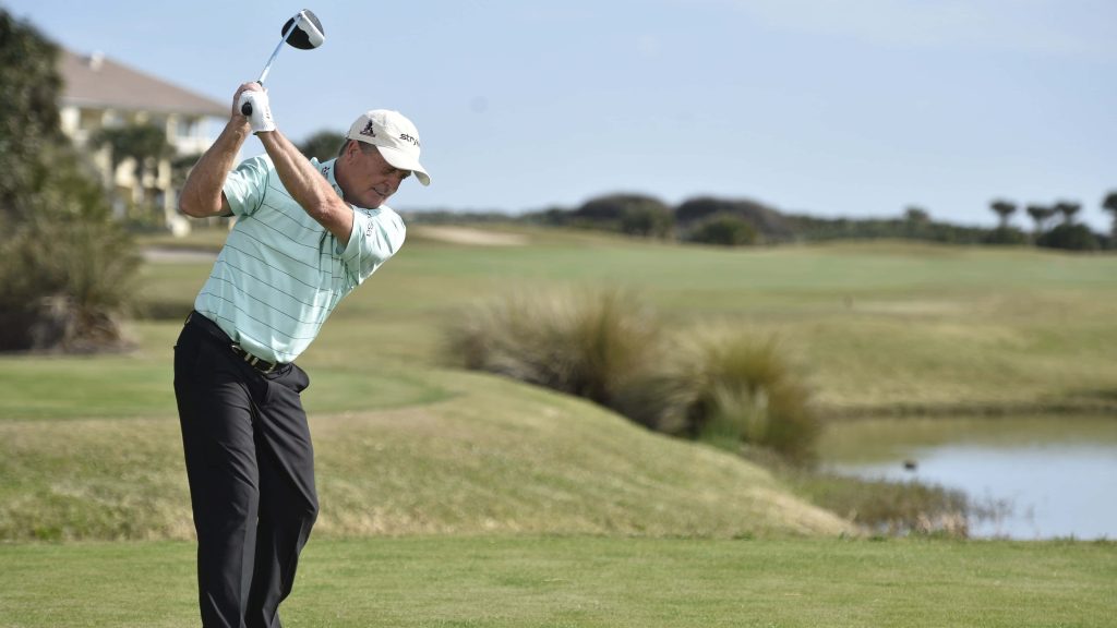 Fred Funk mid-swing on golf course with water hazard wearing blue striped polo and black pants Wallpaper