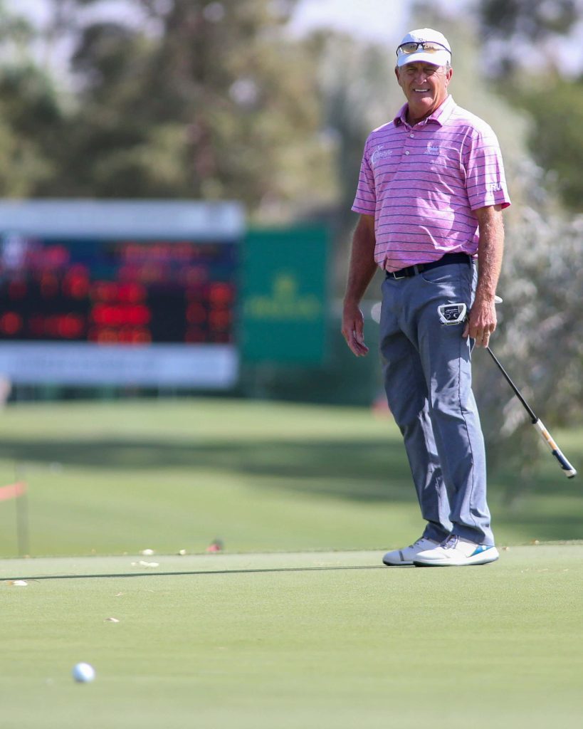 Fred Funk in pink striped polo holding putter on golf green with soft-focus tournament background Wallpaper