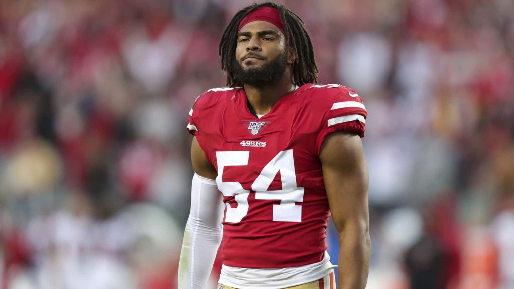 Fred Warner 49ers linebacker focused in red jersey number 54 on field blurred stadium background Wallpaper
