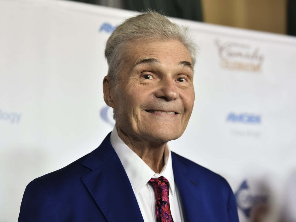 Fred Willard smiling in blue suit and patterned tie at professional event vibrant wallpaper