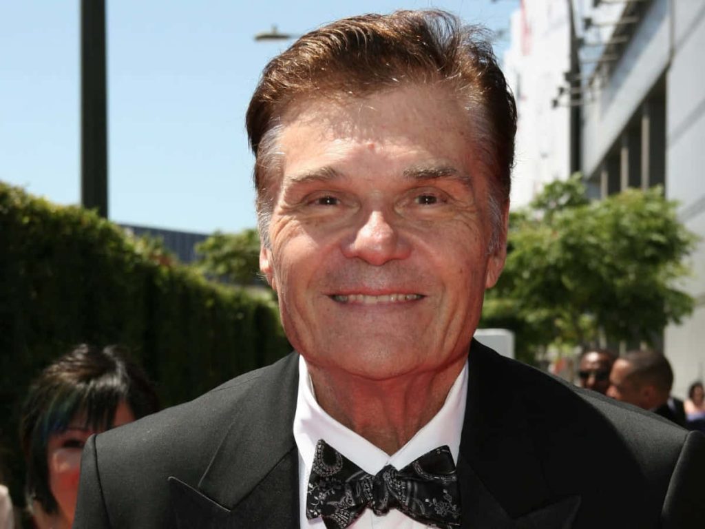 Fred Willard smiling warmly in black tuxedo and patterned bow tie at outdoor red carpet event Wallpaper