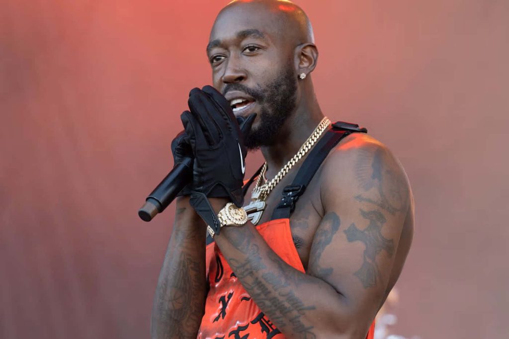 Freddie Gibbs live rap performance intense stage shot orange top black gloves gold jewelry Wallpaper