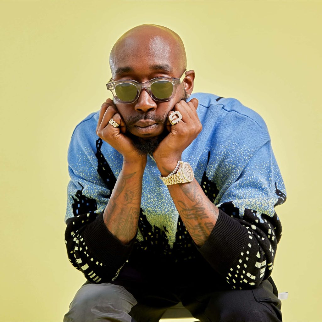 Portrait of rapper Freddie Gibbs in sunglasses with tattoos wearing blue black sweater on yellow background Wallpaper
