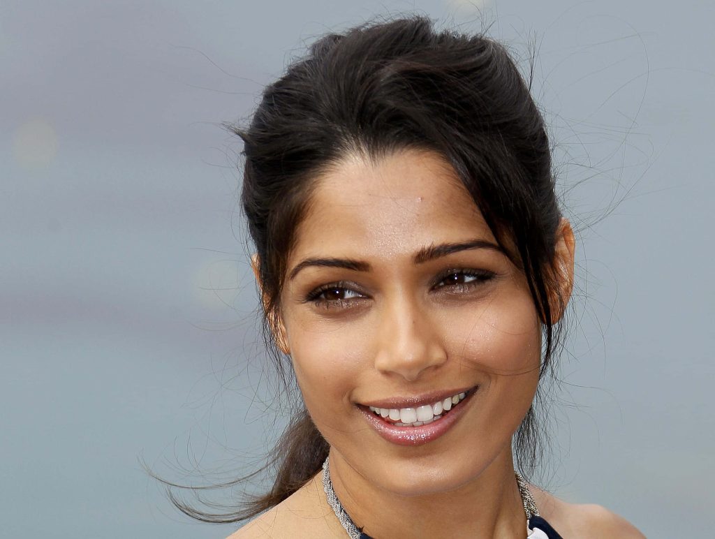 Freida Pinto smiling with windblown ponytail natural makeup soft lighting neutral background portrait Wallpaper