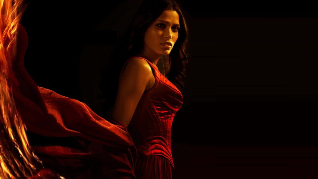 Freida Pinto in vibrant red dress with dramatic warm lighting on dark moody background wallpaper