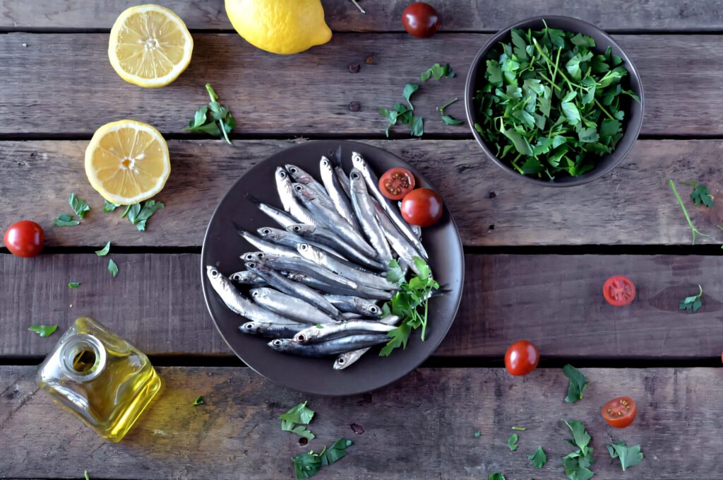 Fresh anchovies on plate with herbs lemon cherry tomatoes and greens rustic wallpaper background