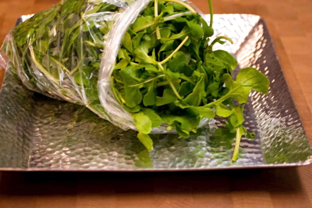 Fresh arugula leaves in clear plastic bag on textured metal tray healthy kitchen wallpaper
