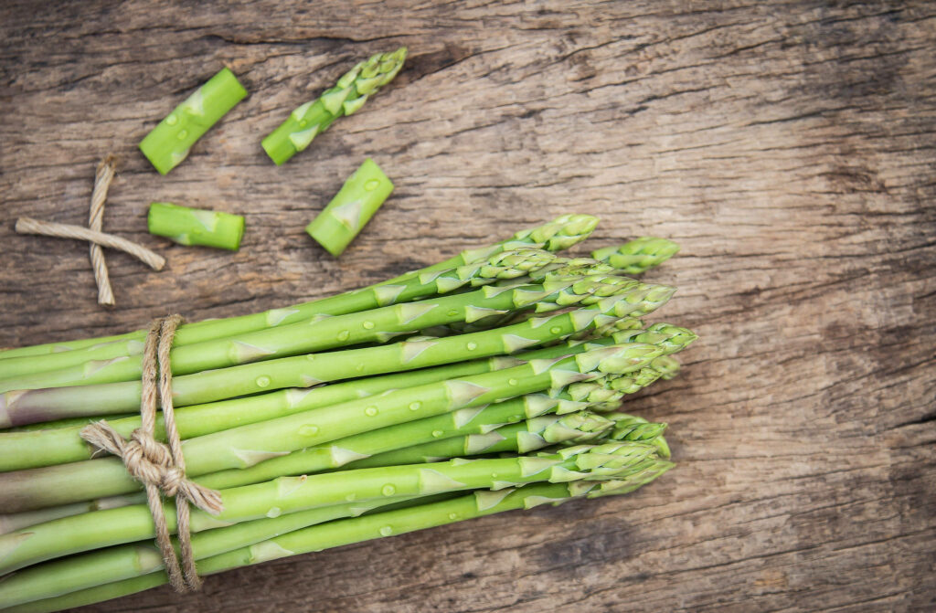 Bundle of fresh asparagus tied with brown rope on rustic wooden surface with cut pieces nearby Wallpaper