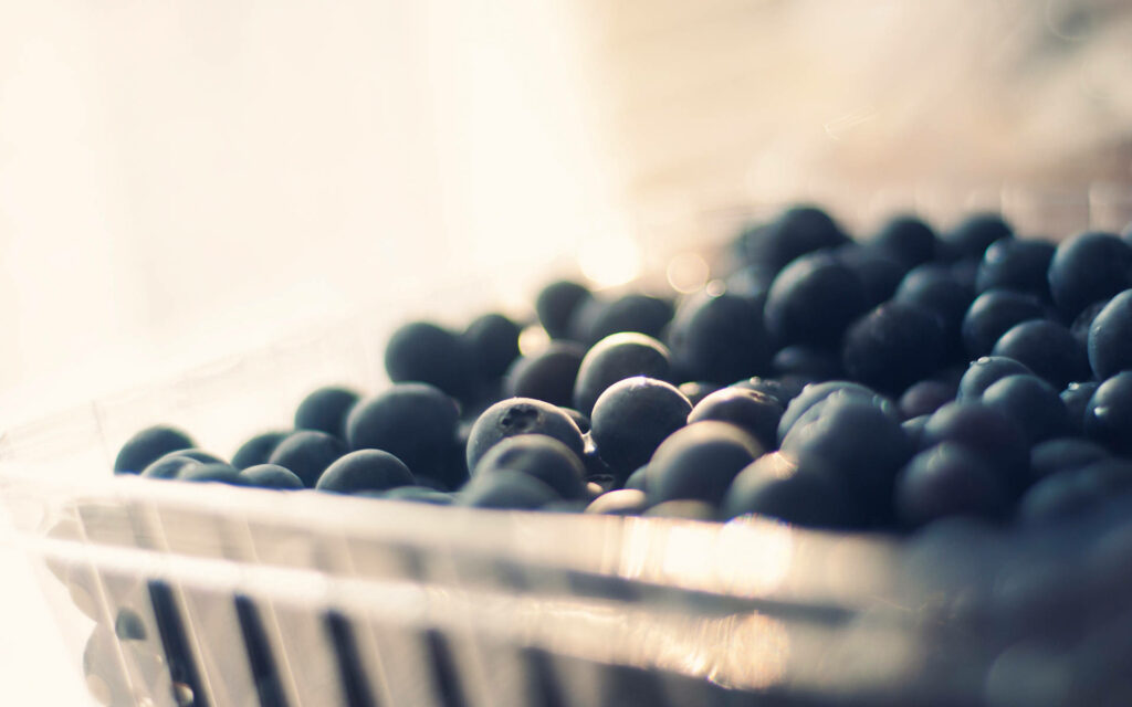 Close-up of fresh blueberries in clear plastic tray with soft natural light wallpaper background