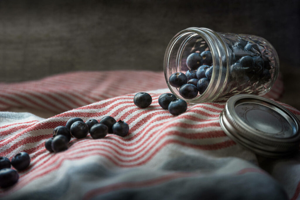 Fresh blueberries spilling from a glass jar onto striped cloth rustic kitchen scene wallpaper background