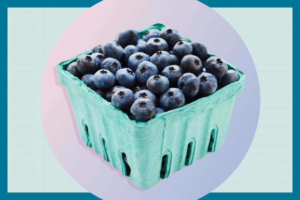 Green box of fresh blueberries on soft pink background vibrant colorful wallpaper image