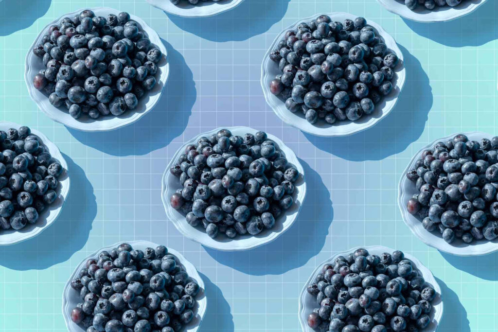 Fresh blueberries in white bowls arranged on pastel blue grid background vibrant pattern Wallpaper