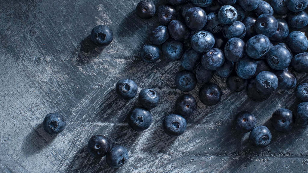 Fresh vibrant blueberries scattered on rustic dark wooden table with natural texture background Wallpaper